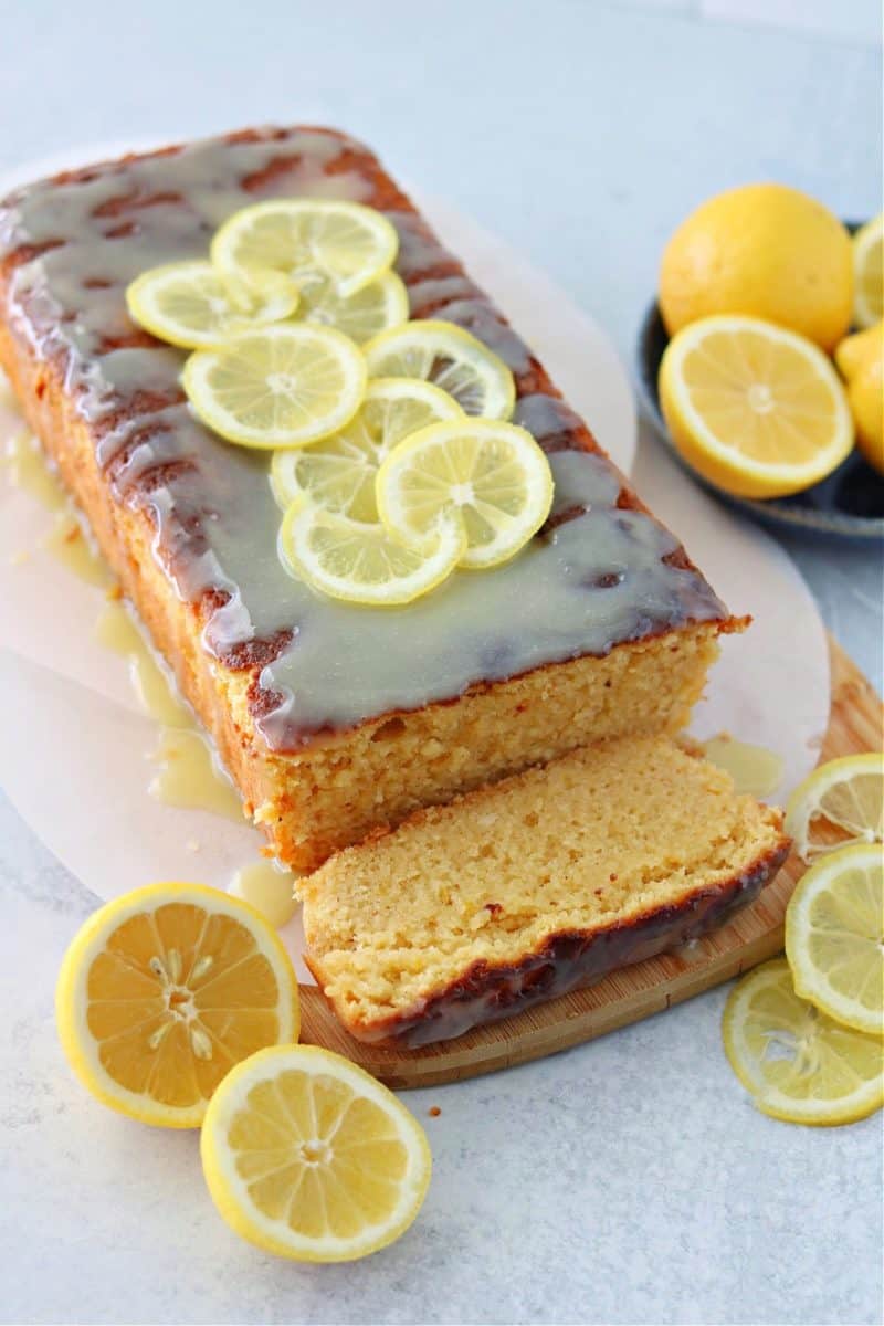 vertical image of keto lemon pound cake on top of a brown cutting board with a keto white chocolate glaze