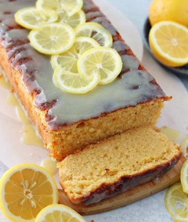 a close up of keto lemon cake with lemons topped with a sugar-free white chocolate glaze on top of a brown cutting board