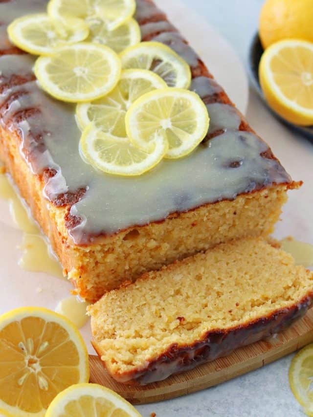 a close up of keto lemon cake with lemons topped with a sugar-free white chocolate glaze on top of a brown cutting board