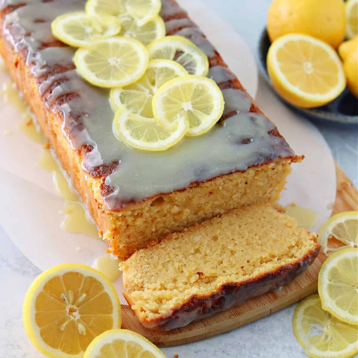 a close up of keto lemon cake with lemons topped with a sugar-free white chocolate glaze on top of a brown cutting board