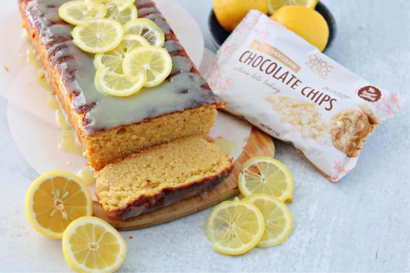 keto lemon pound cake with lemon slices on a brown cutting board with choczero sugar-free white chocolate chips