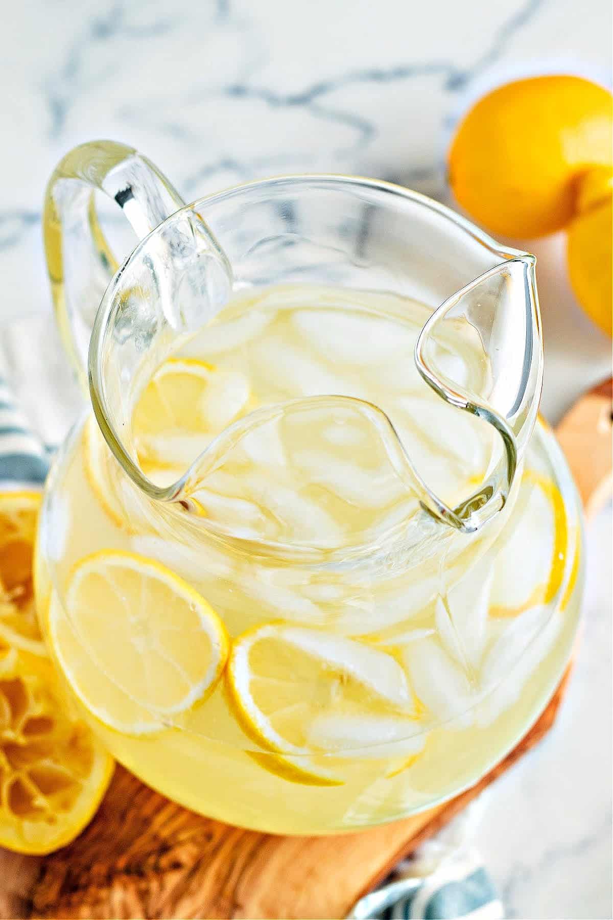 a pitcher of keto lemonade with ice and lemon slices surrounded by fresh lemons