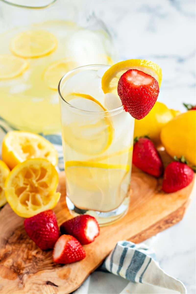 a close-up of glass of keto lemonade on a wooden board with lemon slices and strawberries
