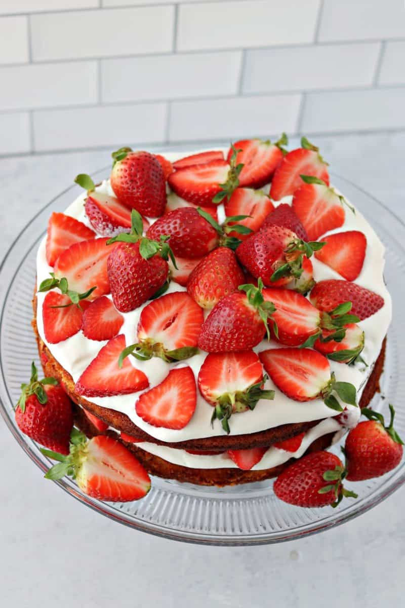 double layer low carb strawberry shortcake on a cake stand with keto whipped cream and fresh strawberries