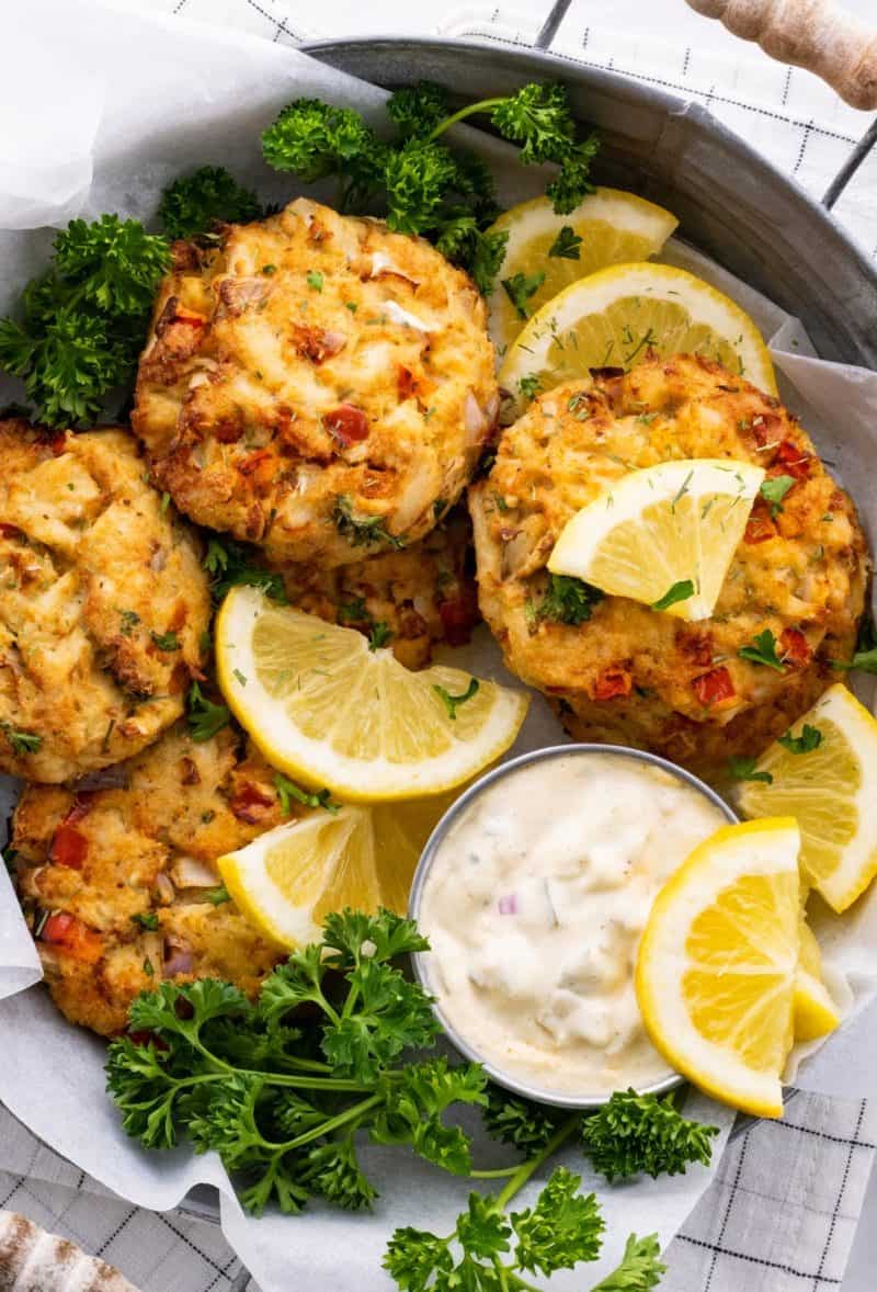 air fryer keto crab cakes in a metal bowl with parsley, lemon, and tartar sauce