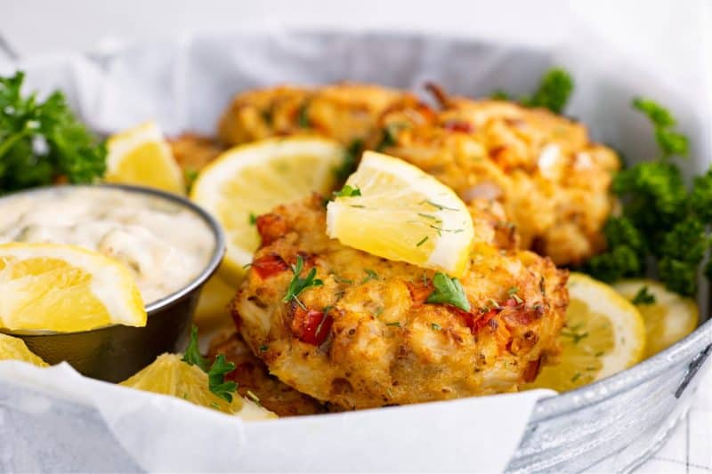 air fryer crab cakes in a metal bowl with tartar sauce and a lemon slice on top