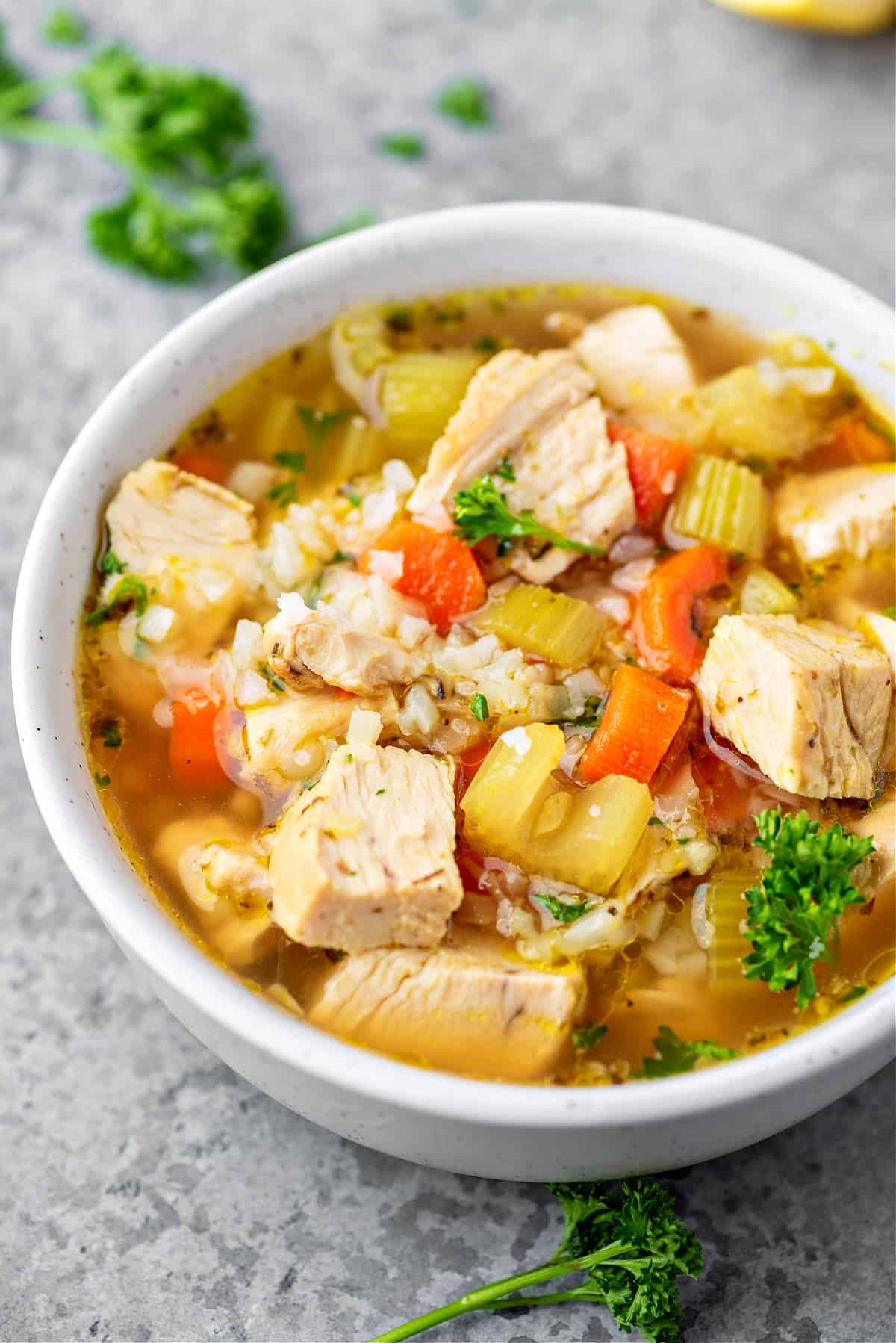 a bowl of keto chicken and vegetable soup with parsley, chicken chunks, celery, carrots and cauliflower rice