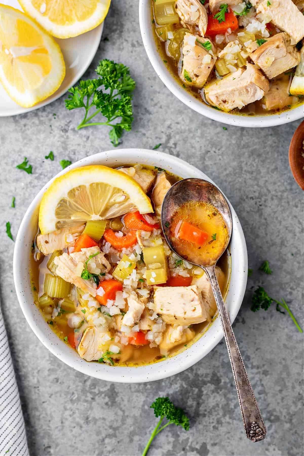 two bowls of keto chicken soup with cauliflower rice, parsley, and lemon slices