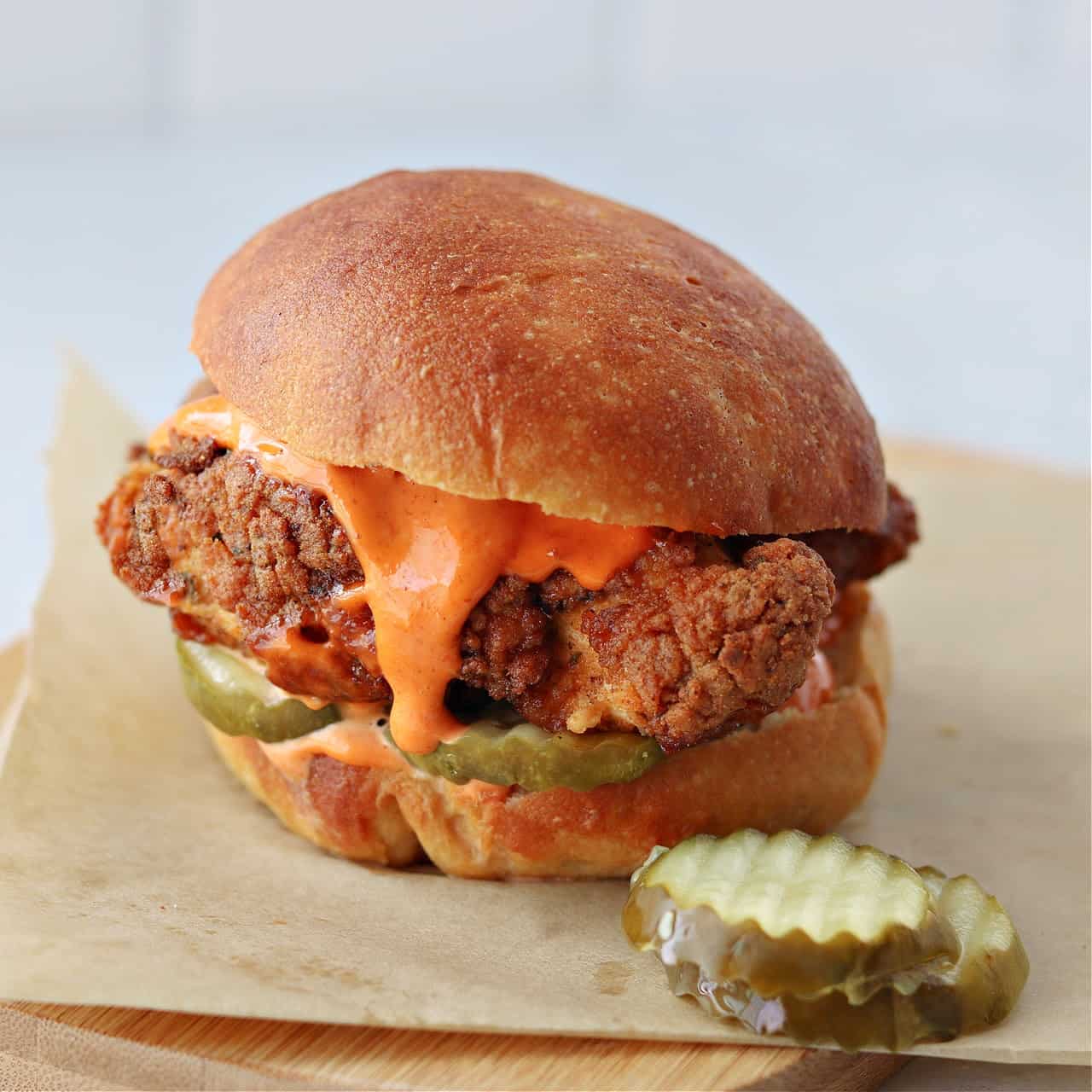 low-carb copycat Popeye's spicy chicken sandwich on brown parchment paper with pickles and spicy mayo dripping out