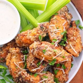 Overhead view of a plate of wings topped with chopped parsley, next to a bowl of ranch and some celery sticks