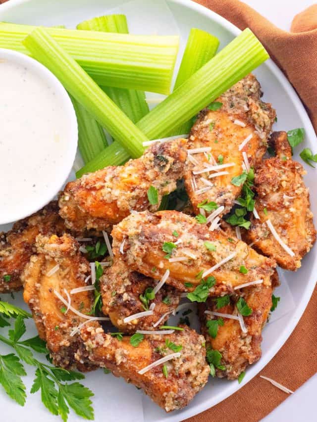 Overhead view of a plate of wings topped with chopped parsley, next to a bowl of ranch and some celery sticks