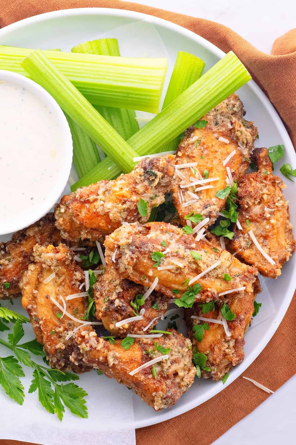 Overhead view of a plate of wings topped with chopped parsley, next to a bowl of ranch and some celery sticks