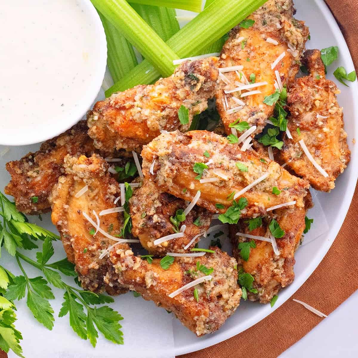Close up of wings on a plate, garnished with parsley, next to a bowl of ranch and some celery sticks