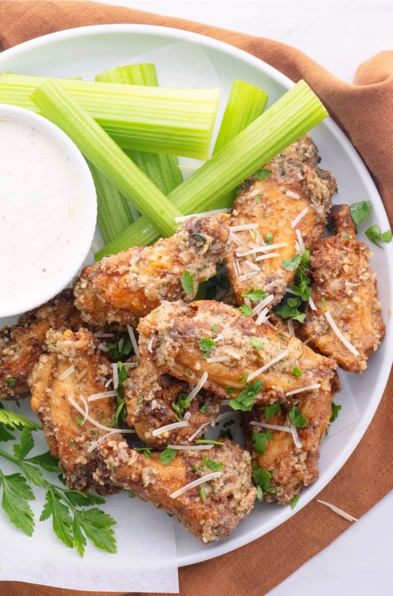 a plate of air fryer garlic parmesan wings on a plate with ranch dipping sauce and celery