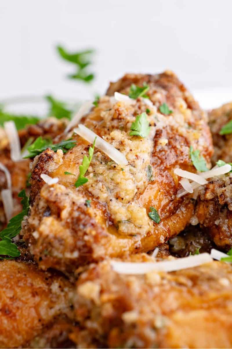 a close-up of a garlic parmesan wing on a plate with parsley and parmesan shreds on top