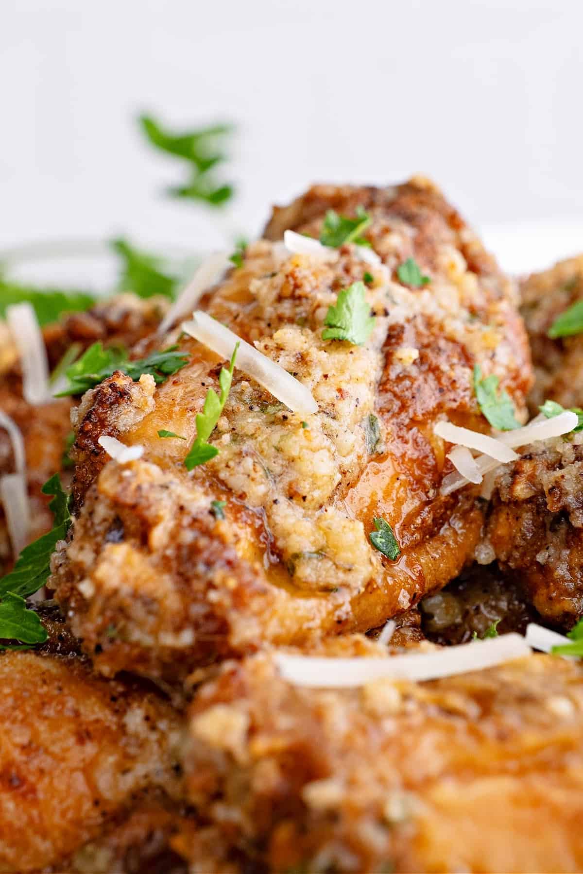 Close up of a wing, on top of a pile of wings, topped with parsley and parmesan cheese