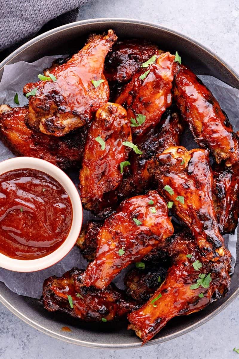 air fryer bbq chickens in a metal pan with a side of keto bbq sauce