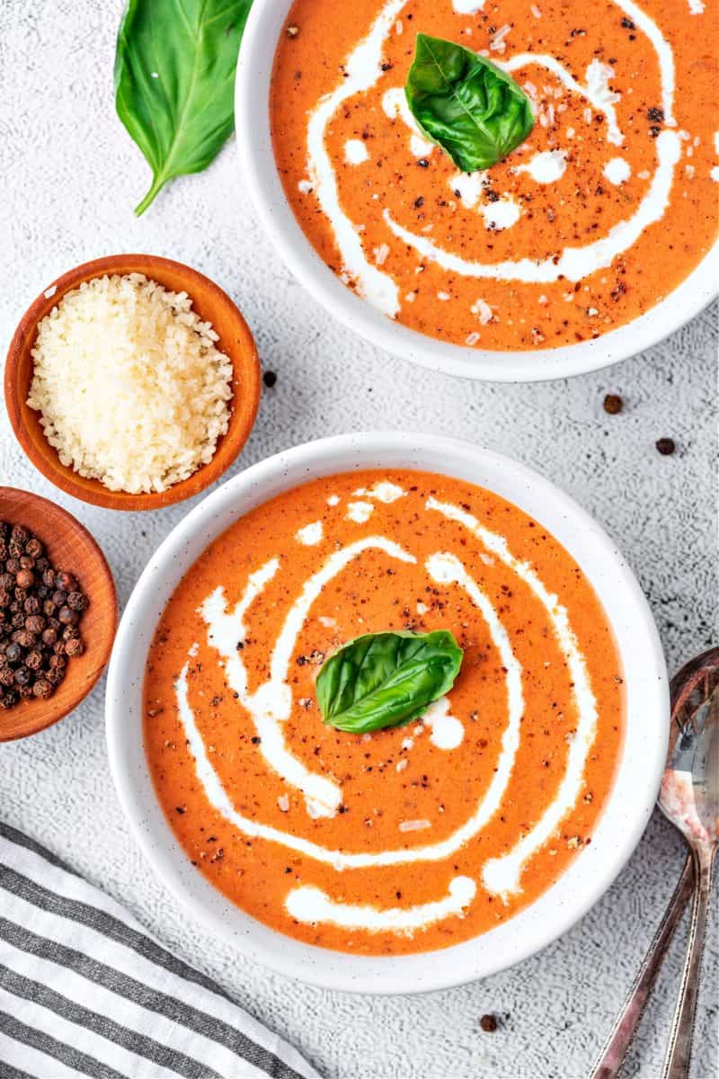 two bowls of keto tomato soup with parmesan and black peppercorns on the side