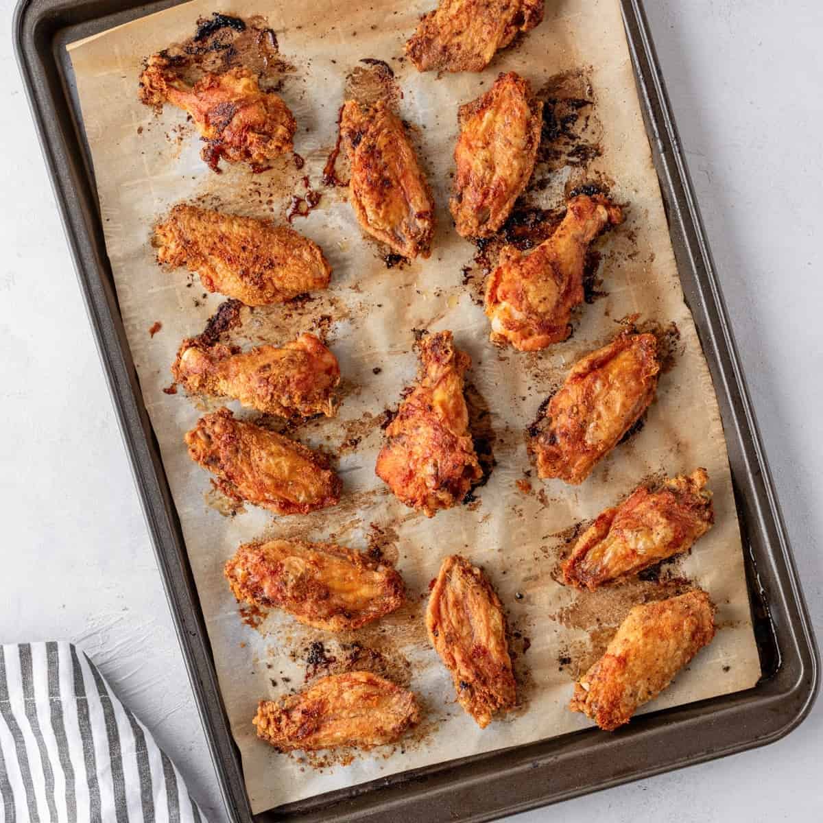 Overhead view of a baking tray with parchment paper and 15 baked wings on it