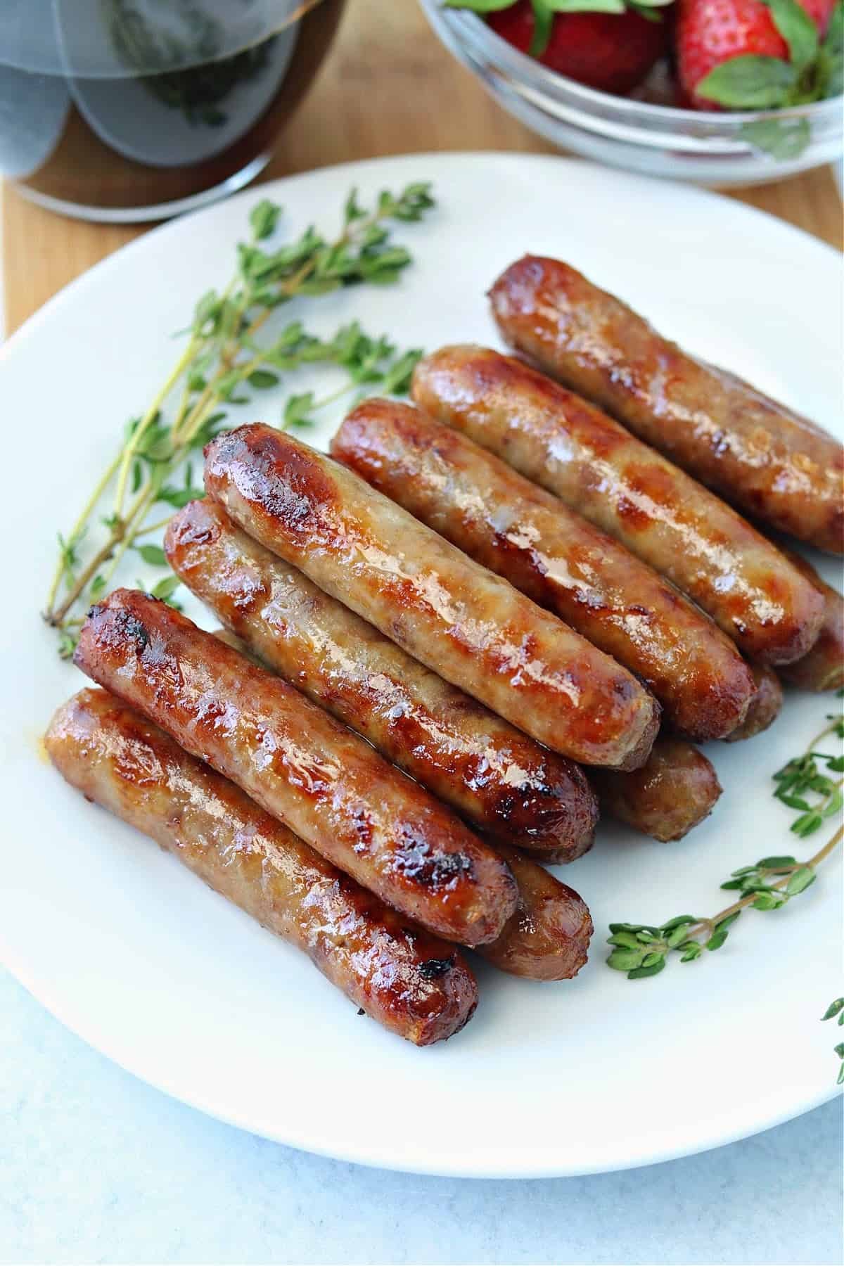 A plate of air fryer breakfast sausages next to a cup of coffee and a bowl of strawberries.