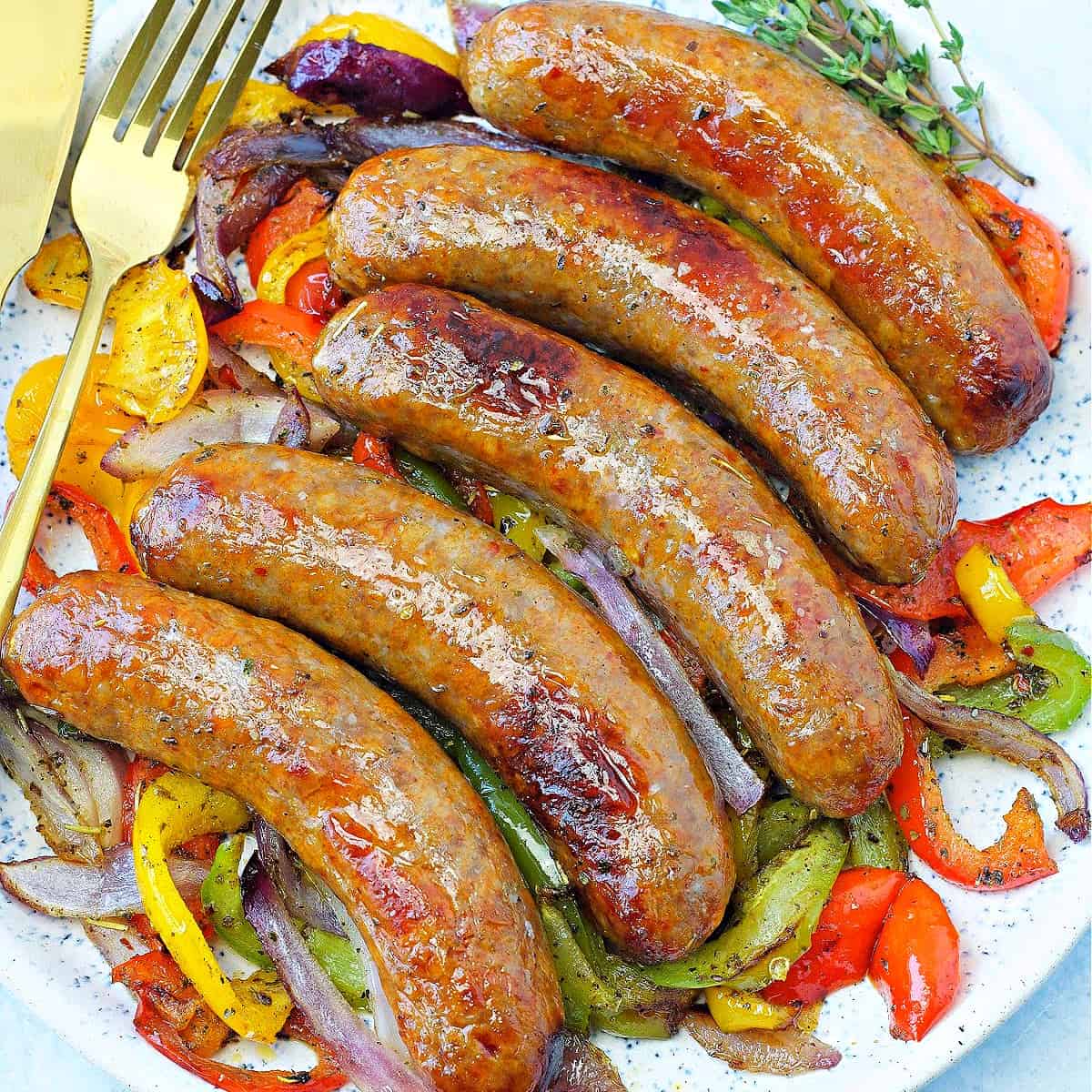 close-up of five air fried Italian sausages on a plate with sautéed peppers and onions
