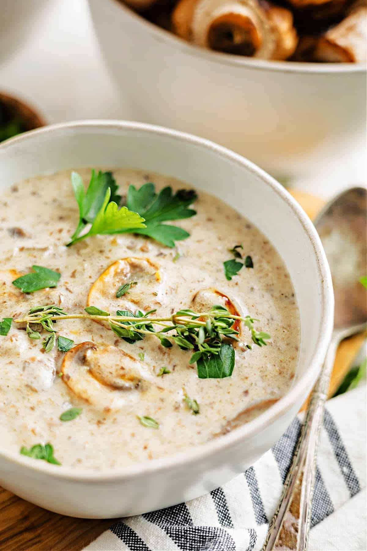 a bowl of keto cream of mushroom soup with a spoon and fresh herbs like fresh thyme.