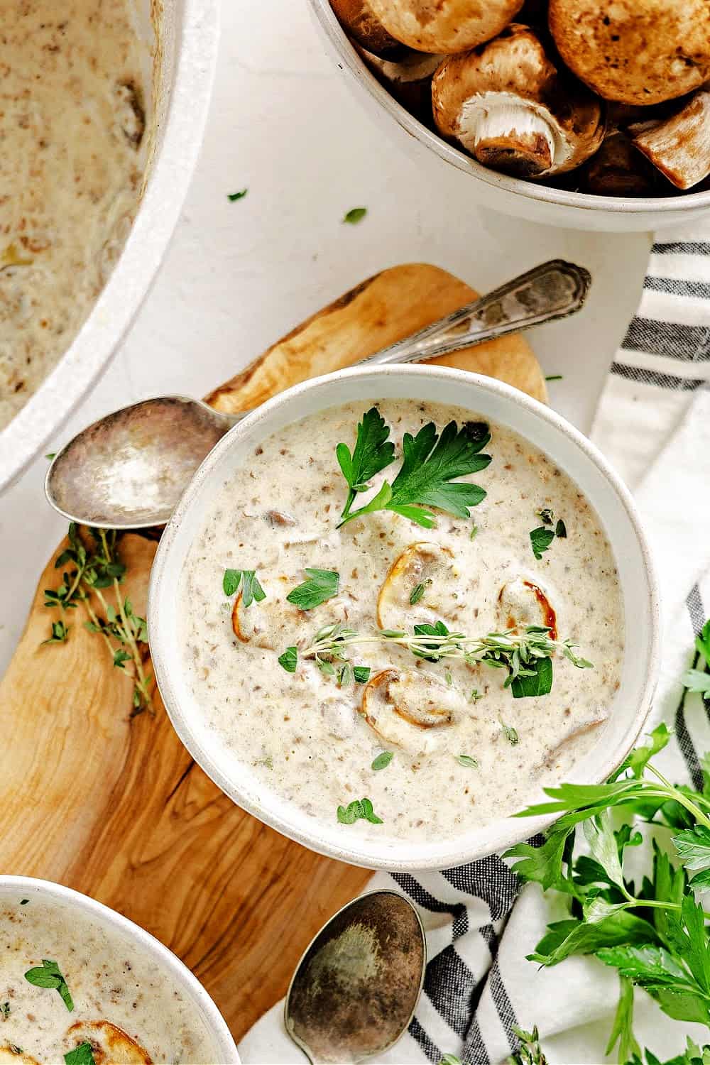 a bowl of keto cream of mushroom soup next to pot of soup with thyme sprigs and parsley