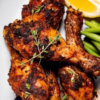 close up of air fryer dry rub chicken legs on a plate with lemon and a green vegetable