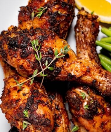 close up of air fryer dry rub chicken legs on a plate with lemon and a green vegetable