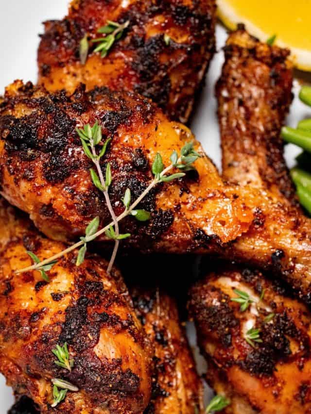 close up of air fryer dry rub chicken legs on a plate with lemon and a green vegetable