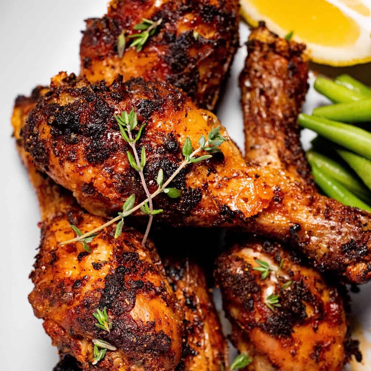 close up of air fryer dry rub chicken legs on a plate with lemon and a green vegetable