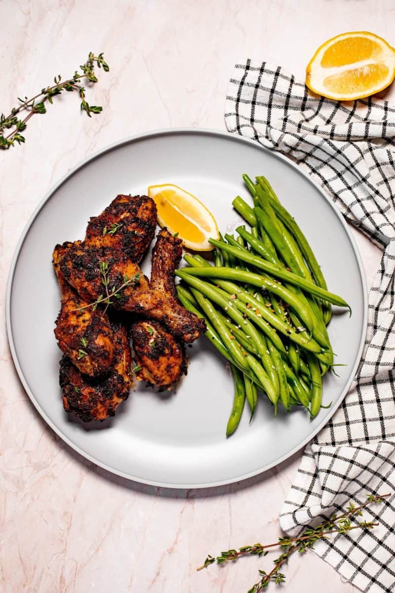 air fryer dry rub chicken drumsticks on a plate with lemon and a green beans