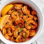 close up of air fryer cajun shrimp in a bowl with parsley and lemon wedges