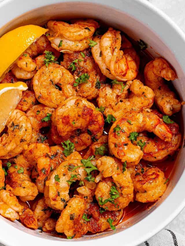 close up of air fryer cajun shrimp in a bowl with parsley and lemon wedges