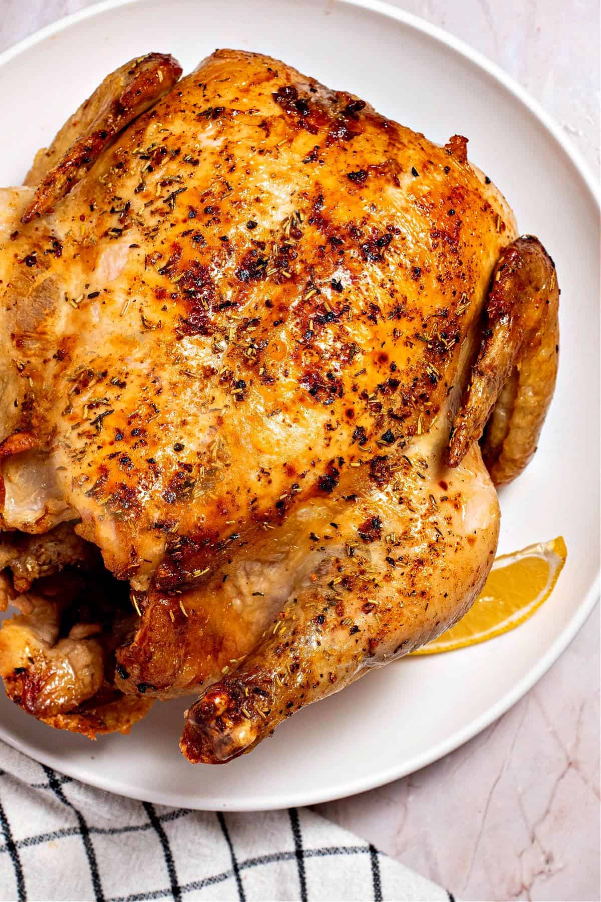 A season roast chicken on a plate with a lemon slice