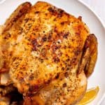 Close up of a roast chicken on a plate with a lemon slice