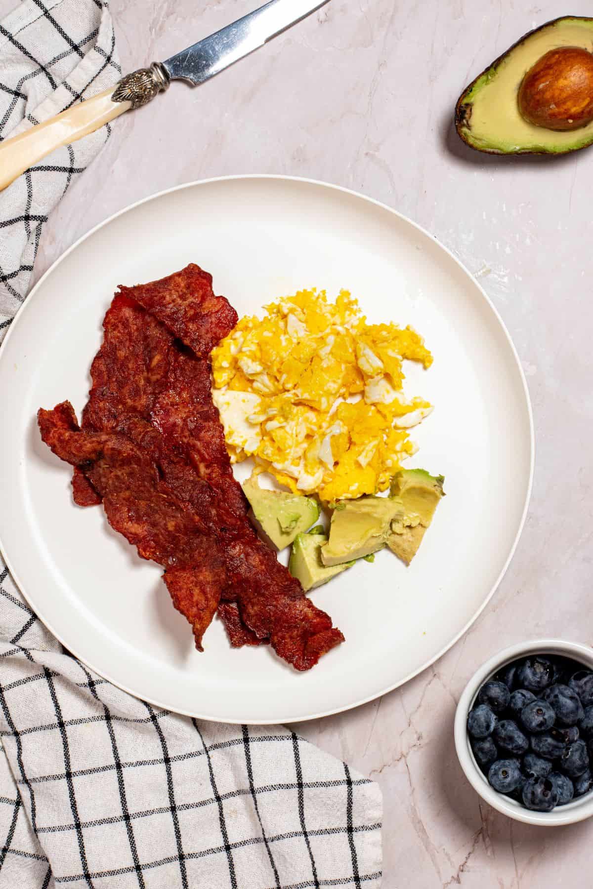 crispy air fried turkey bacon with fried egg and avocado slices on a large white plate