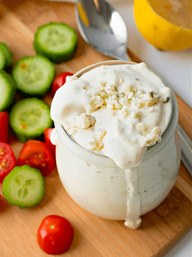 Blue Cheese Dressing in a glass jar with sliced tomatoes, cucumbers and lemon