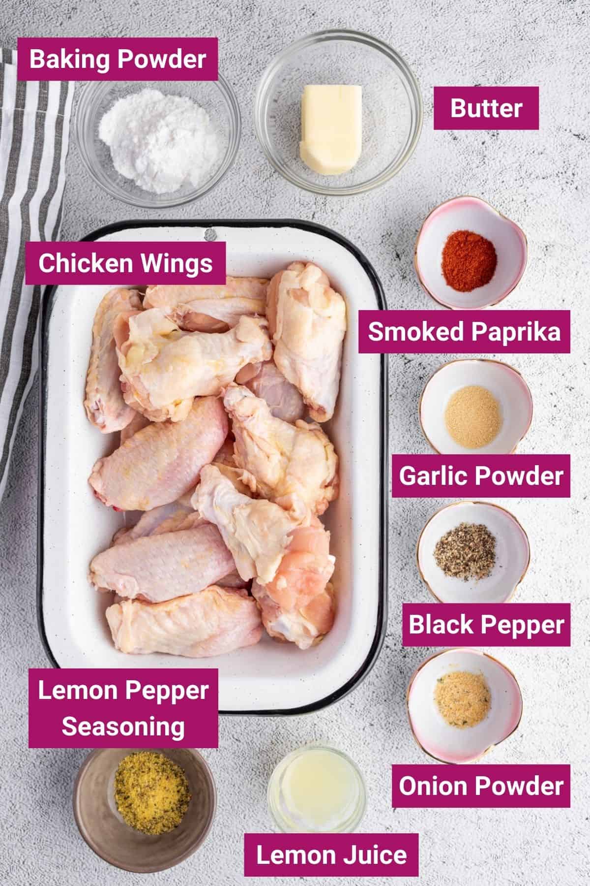 These lemon pepper chicken wings are crispy on the outside and juicy on the inside, plus they're super easy to make! Overhead view of the labeled ingredients needed for lemon pepper wings: a tray of raw chicken wings, a bowl of baking powder, a bowl of butter, a bowl of smoked paprika, a bowl of garlic powder, a bowl of black pepper, a bowl of onion powder, a bowl of lemon juice, and a bowl of lemon pepper seasoning.