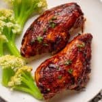 two air fryer bbq chicken breasts on a plate with caulilini