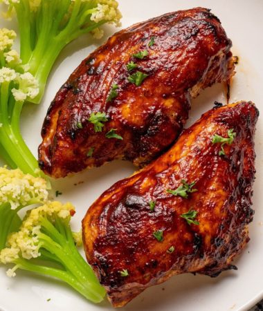 two air fryer bbq chicken breasts on a plate with caulilini