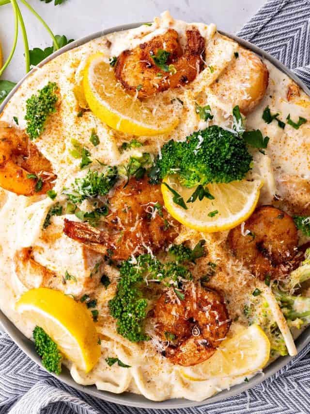 close up of cajun shrimp alfredo pasta in a bowl with broccoli, parsley and lemon wedges