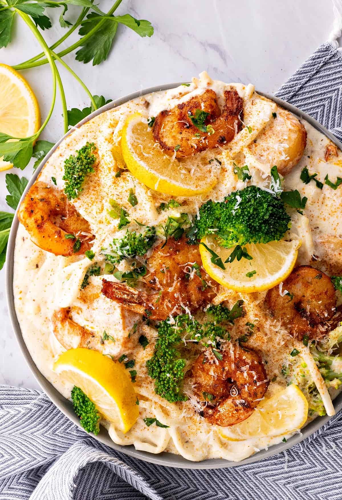 cajun shrimp alfredo pasta in a bowl with broccoli, parsley and lemon wedges