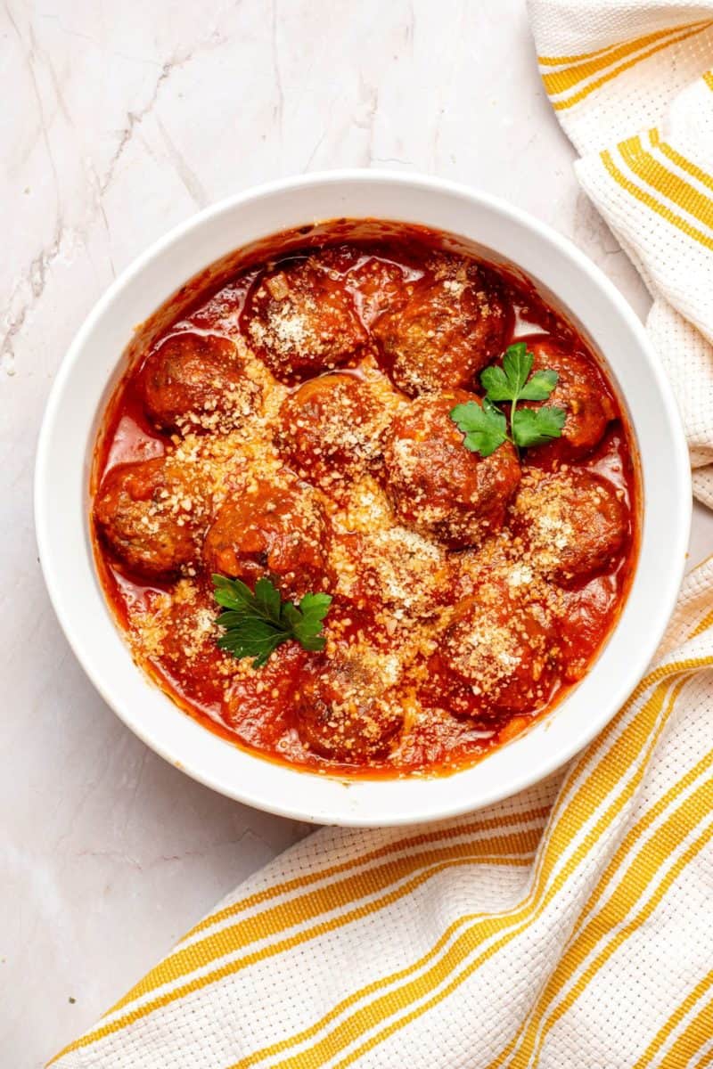 Frozen Meatballs with marinara sauce topped with parsley and cheese on a large bowl