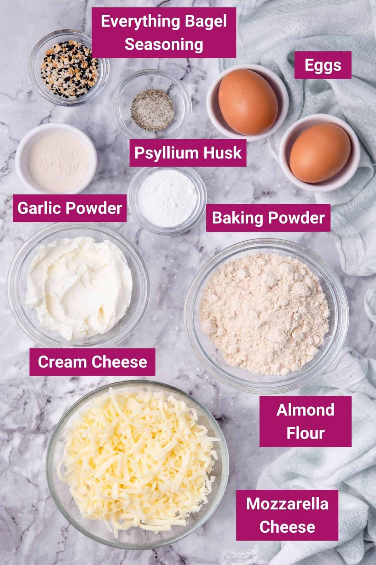 ingredients needed to make a keto bagel like almond flour, baking powder, garlic powder, eggs, cream cheese, mozzarella cheese and psyllium husk on separate bowls