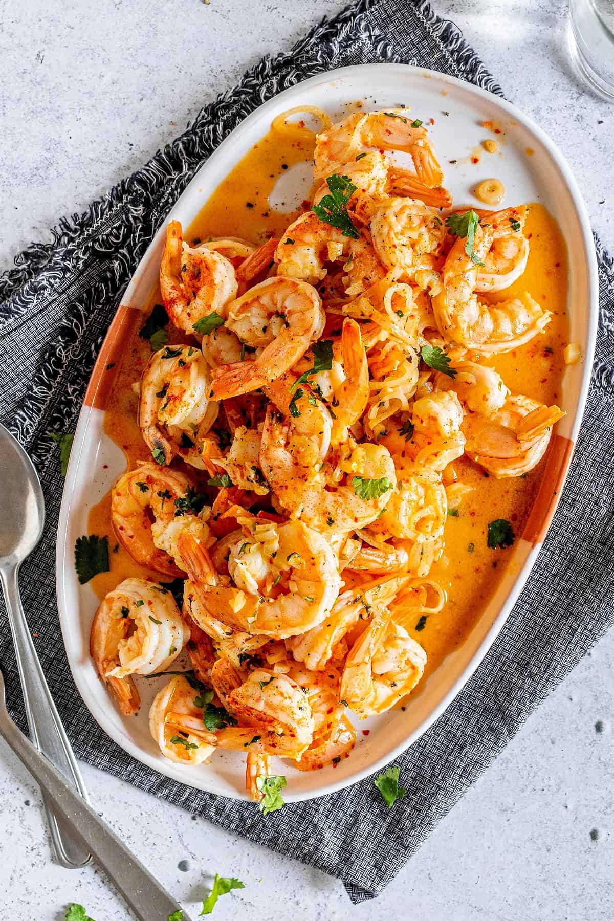 low carb Shrimp Scampi recipe cooked on a on a plate with fresh parsley, shallots, cooked garlic cloves and shrimp scampi sauce.