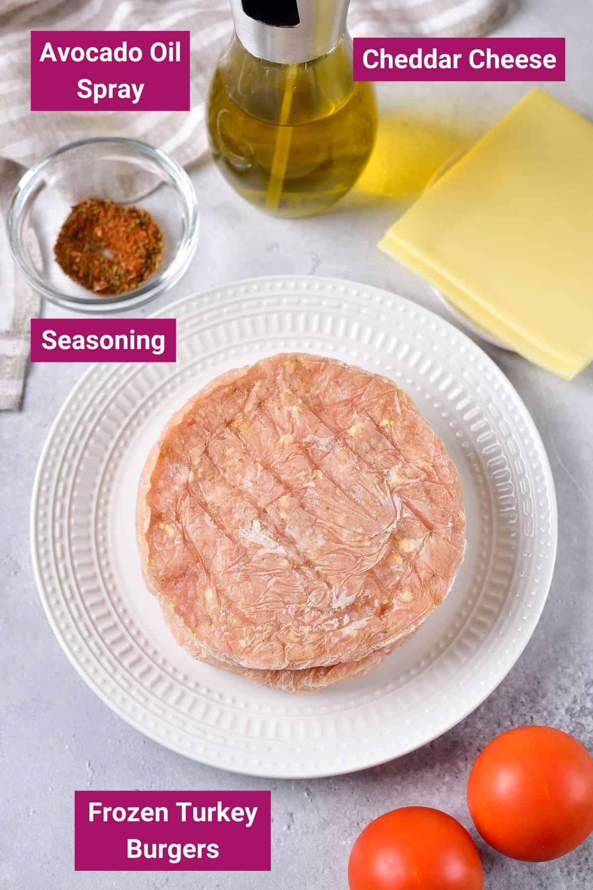 ingredients to make frozen turkey burger patties in an air fryer on a plate: frozen turkey burgers, avocado oil spray, seasoning and cheddar cheese