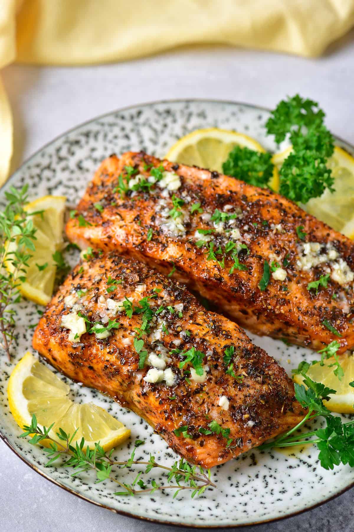 Two fillets of salmon on a plate with lemons and herbs, and garnished with parsley.