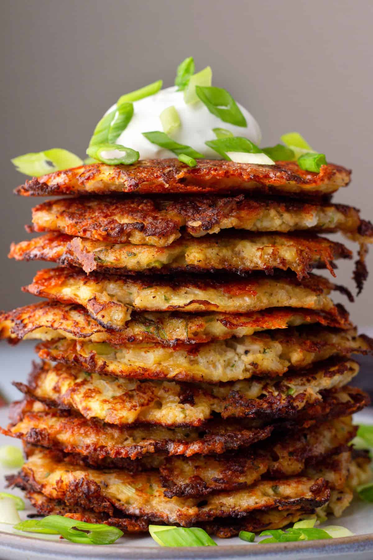 stacked Cauliflower Hash Browns on a plate with green onions and sour cream