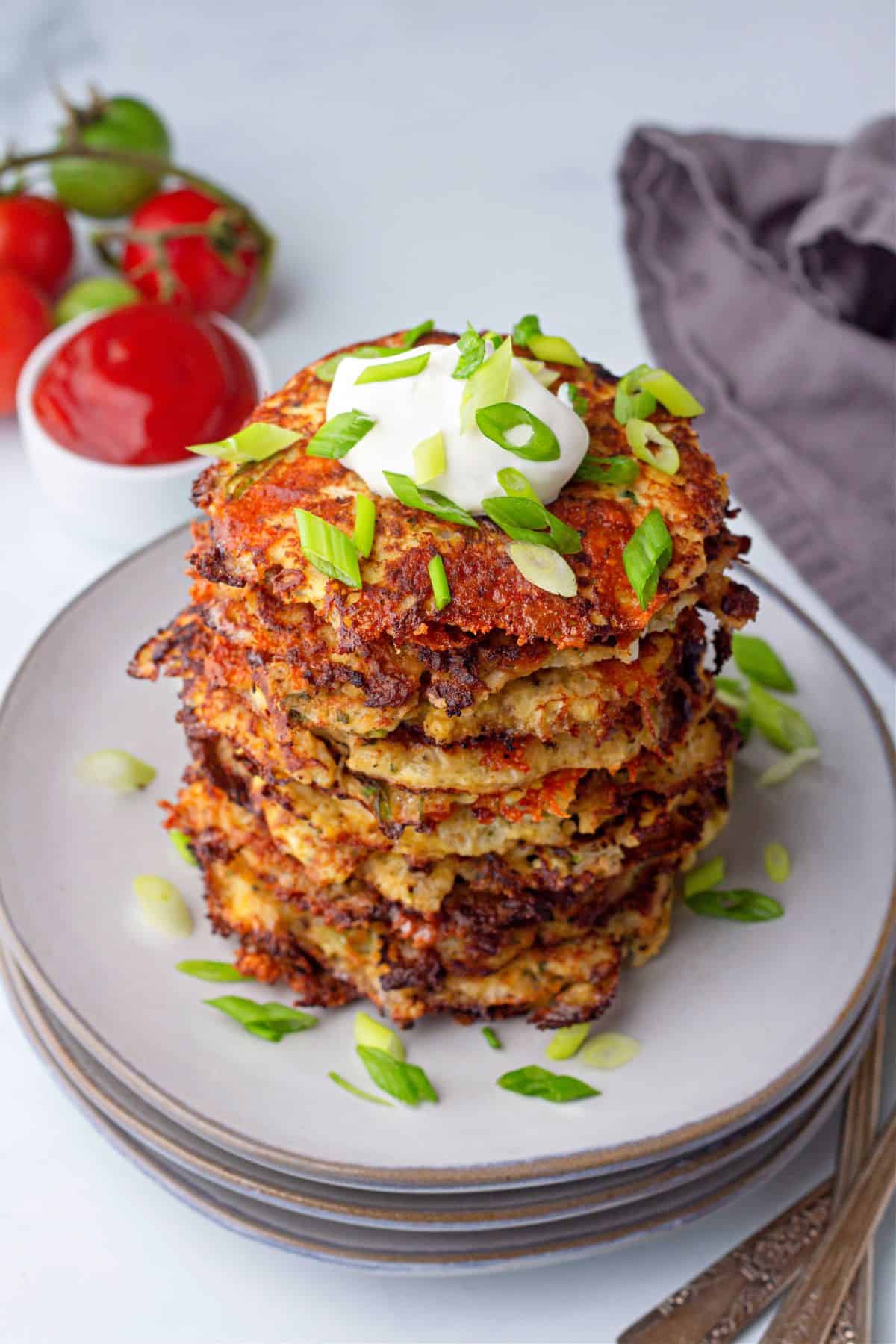 stacked Cauliflower Hash Browns on a plate with a cup of homemade sugar free ketchup on the side.